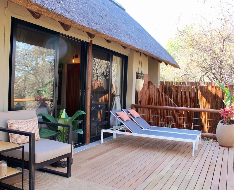 The deck of a tented suite with loungers and a daybed under a thatched roof