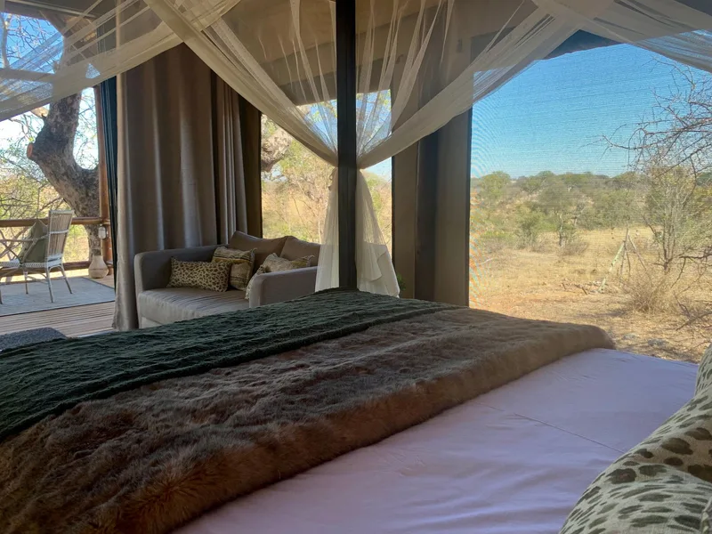 A made-up bed under a mosquito net, looking out through mesh to the bush beyond