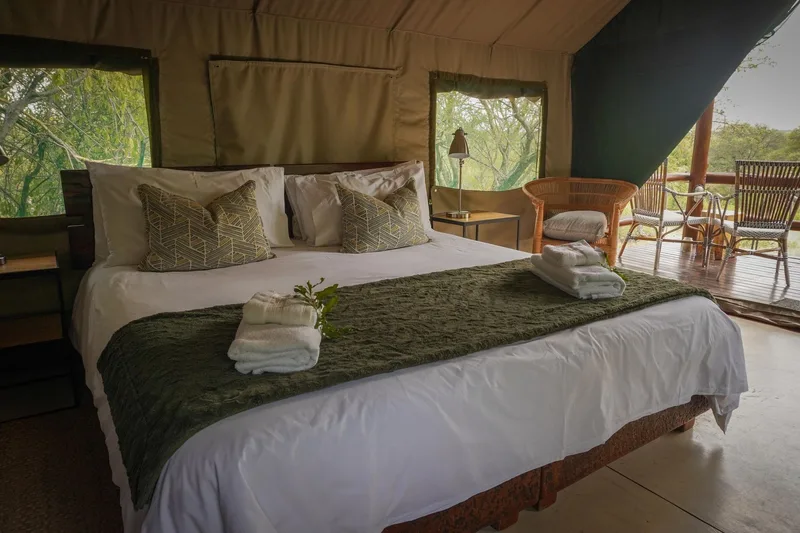 A tented suite bedroom with a made-up double bed and armchair by the window