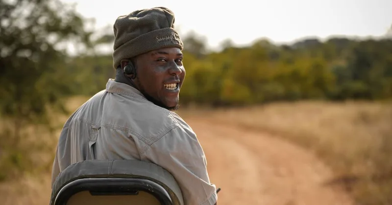 A smiling guide in a safari hat looking back over his shoulder from the vehicle