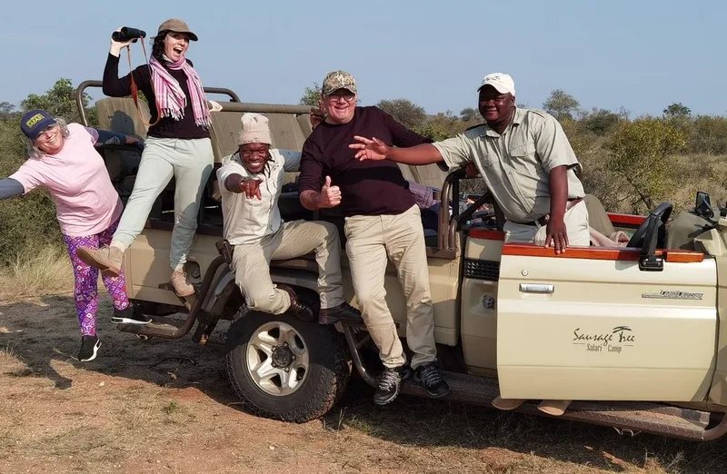 A family posing together beside an open safari vehicle with their guide
