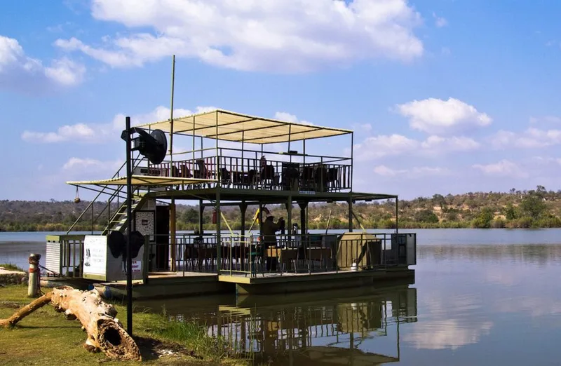 A double-decker river cruise boat moored on the Blyde Dam under a blue sky