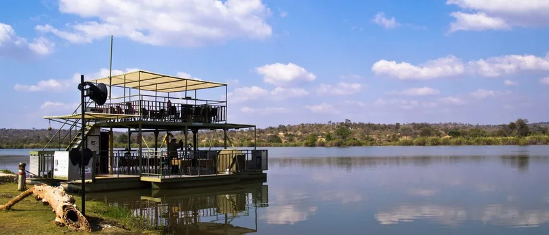 A double-decker river cruise boat on calm water under a blue sky
