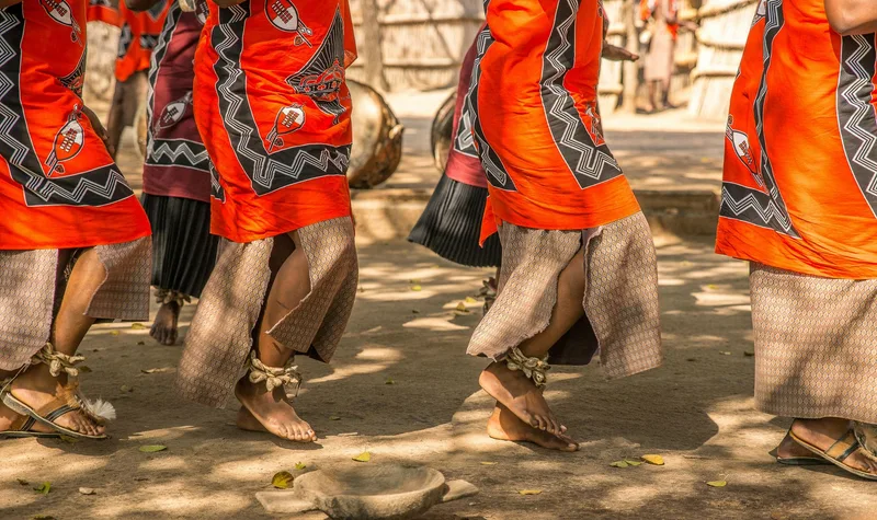 Dancers in bright orange and red traditional skirts, seen from the waist down mid-step