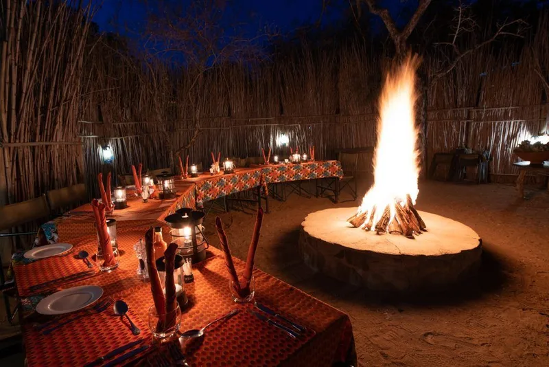 The boma at night, guests dining around a central open fire under a reed roof