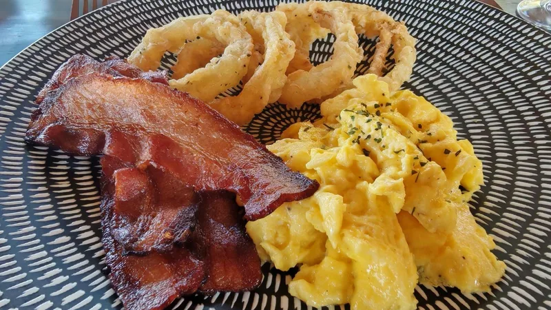 A breakfast plate of bacon, scrambled egg and onion rings